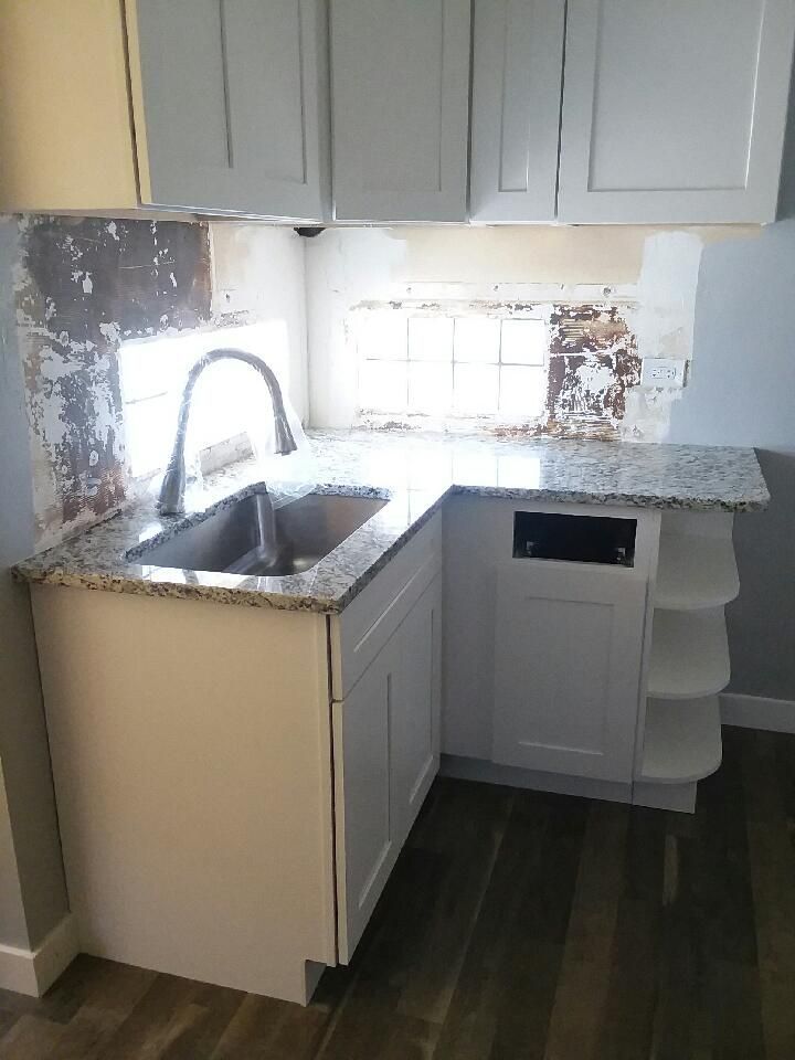 White kitchen sink and cabinets with granite countertop. Rustic backsplash.