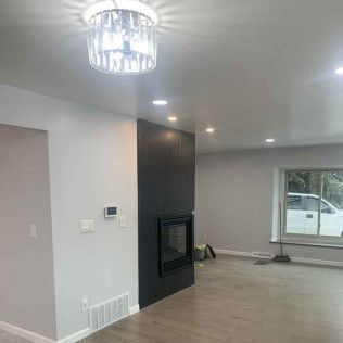 Modern living room with fireplace, gray walls, recessed lighting, and a crystal chandelier.