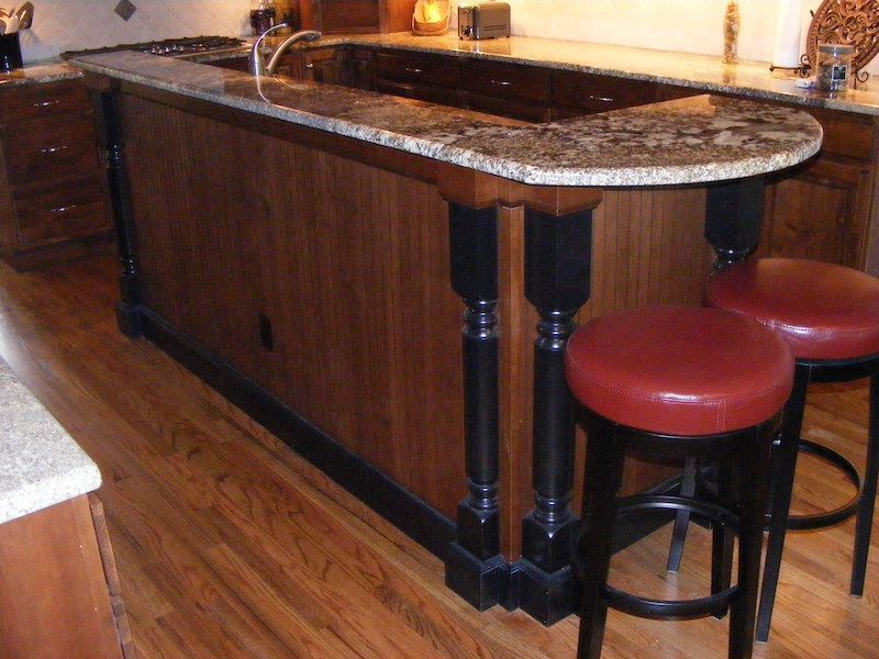 Kitchen island with granite countertop, wood paneling, black accents, and bar stools.