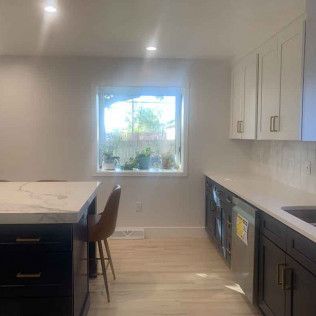 Modern kitchen with white and dark cabinets, marble countertops, and a window.