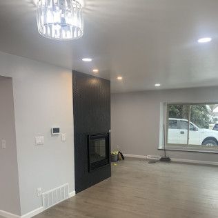 Empty living room with dark fireplace and large window, light gray walls, and recessed lighting.