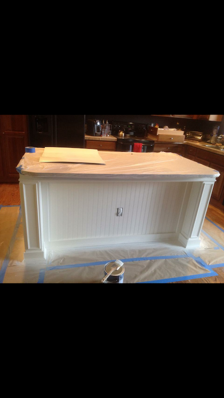 White kitchen island, freshly painted, covered in protective plastic, in a kitchen setting.