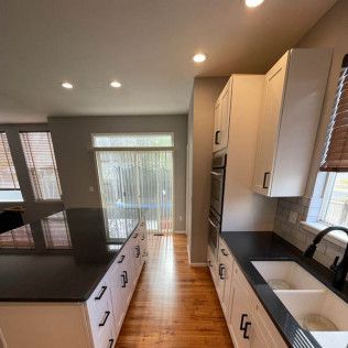Modern kitchen with white cabinets, dark countertops, and hardwood floors.