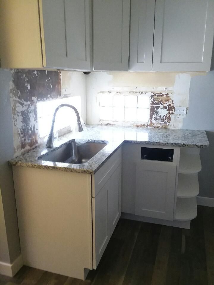 White kitchen cabinets with a stainless steel sink and granite countertop in a corner, with exposed wall behind.