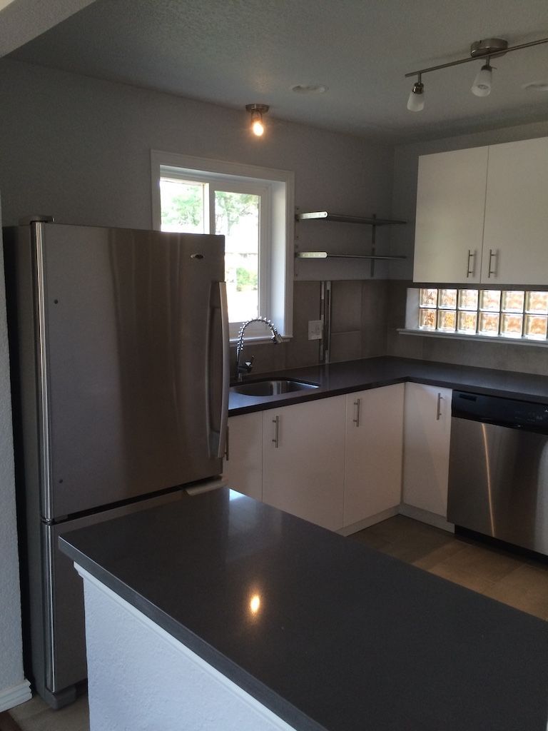 Modern kitchen with stainless steel appliances, white cabinets, and dark countertop.
