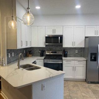 Modern white kitchen with stainless steel appliances, marble countertops, and pendant lighting.