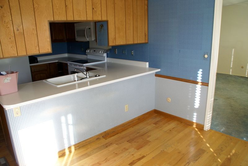 Kitchen with wooden cabinets, blue patterned walls, and white countertop. Hardwood floors.