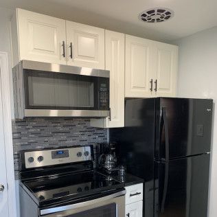 Kitchen with white cabinets, stainless steel microwave and oven, black refrigerator.