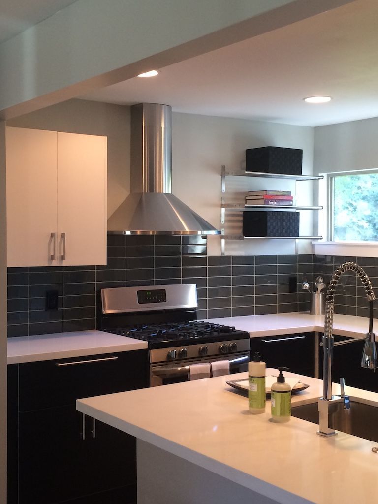 Modern kitchen with white and black cabinets, stainless steel range hood, and white countertops.