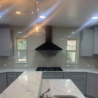 Kitchen with gray cabinets, marble countertops, black range hood, and pendant light.
