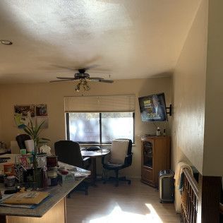A living room with a kitchen island.  A table with chairs in front of a window. A television hangs on the wall.