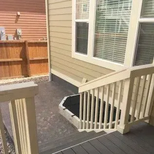 Exterior of a home with a wooden deck, stairs leading down to a basement entrance, and a window.