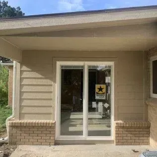 Beige house exterior with sliding glass doors, brick accents, and a covered porch.