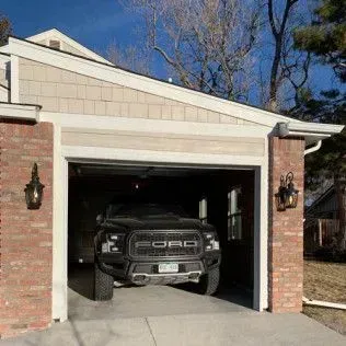 Black Ford truck parked in a garage. Exterior shot of a brick house with a garage and two sconces.