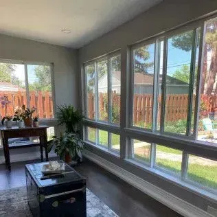 Sunroom with windows overlooking a backyard, table with plants, and a trunk for a coffee table.