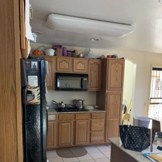 Kitchen with wood cabinets, microwave, fridge, and a large overhead light.