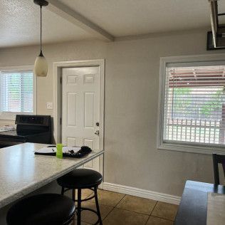 Kitchen with a white countertop, stools, door, and windows.