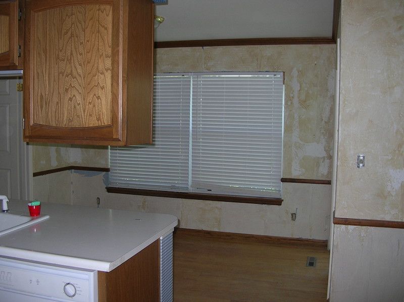 Kitchen with cabinets, countertops, window with blinds, and wood flooring.