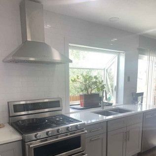 Stainless steel range hood above a gas stove in a bright kitchen with a window and sink.