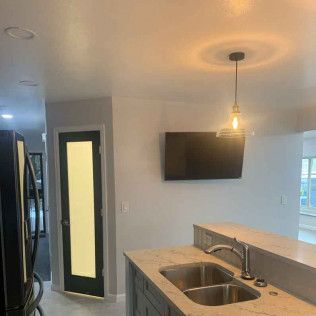 Kitchen with sink, countertop, and mounted TV. A pendant light hangs overhead.