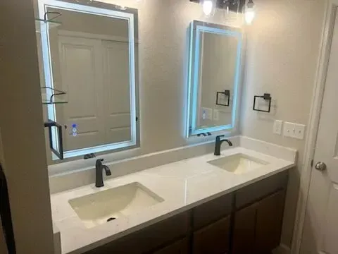 Bathroom with two sinks, two mirrors with led lights, white countertop, and brown cabinets.