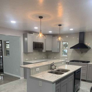 Modern kitchen with gray cabinets, island with sink, and pendant lights.