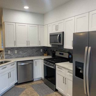 White kitchen cabinets, stainless steel appliances, backsplash, and gray flooring.