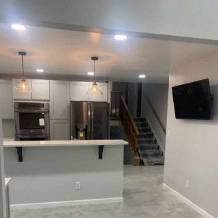 Kitchen with light gray cabinets, stainless steel appliances, and a gray island. A TV hangs on the wall.