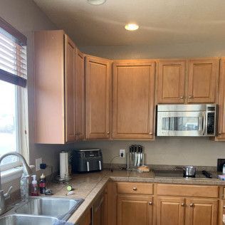 Kitchen with light brown cabinets, sink, window, microwave, and countertop appliances.