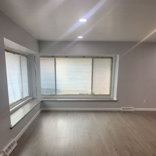 Empty room with large windows, light gray walls, and wood-look flooring.