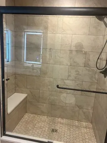 Shower with beige tiles, bench, glass door, black frame, and hex tile floor.
