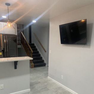 Interior with kitchen, stairs, and a mounted TV on a gray wall.