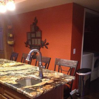 Kitchen island with granite countertop, sink, and seating. Orange wall with decorative shelf.