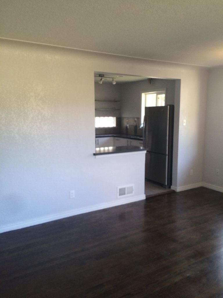 Living room with dark wood floors, light gray walls, and a pass-through to the kitchen with stainless steel appliances.