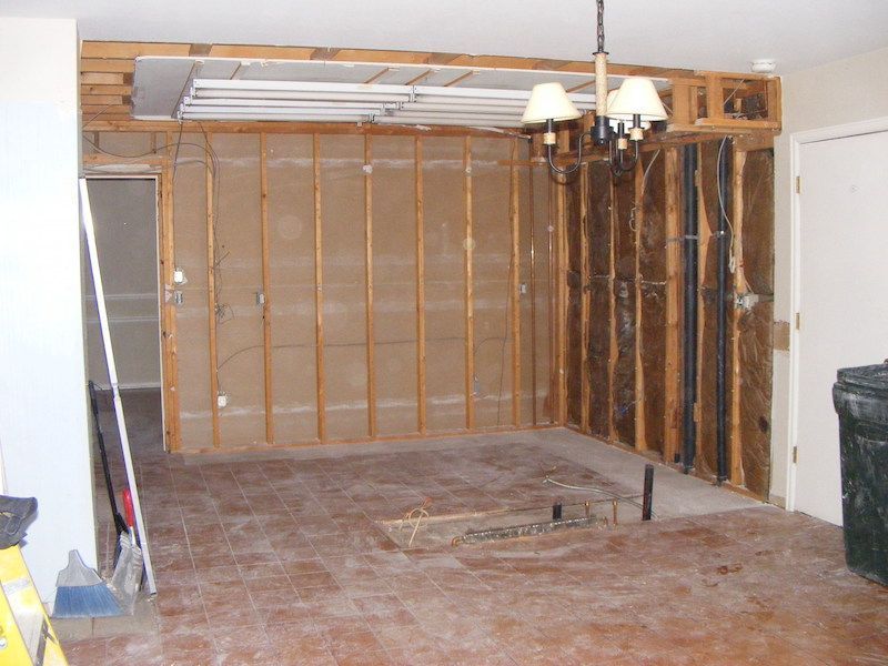 Interior room with exposed studs and unfinished walls, ceiling light fixture, and debris on the floor.