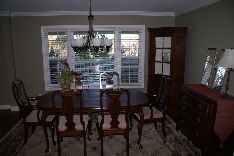 Dining room with oval table, chairs, and china cabinet. Window behind table, chandelier overhead.