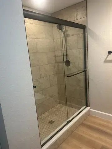 Shower with sliding glass doors, tan tile walls, and light wooden floor.