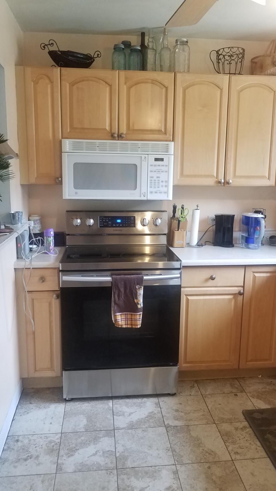 Kitchen with light wood cabinets, stainless steel stove and microwave, and items on counter.