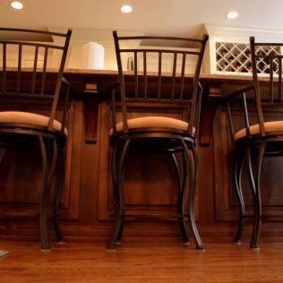 Three bar stools with brown cushions, in front of a wood-paneled bar.