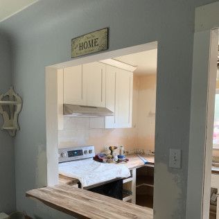 Kitchen interior with a pass-through to a second room. White cabinets, stove, and a wooden counter in view. Light blue walls.