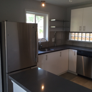 Kitchen with stainless steel appliances, white cabinets, gray countertops, and a window.