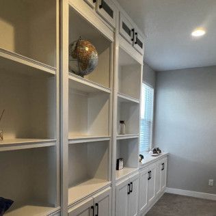 Built-in white bookshelves with a globe and cabinets below, next to a window and gray wall.