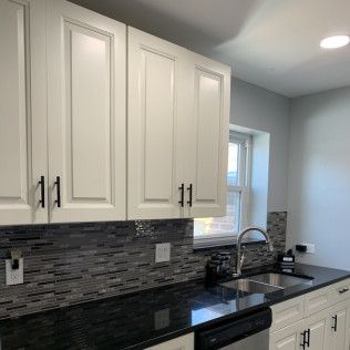 White kitchen cabinets with black hardware above a dark countertop and a mosaic backsplash.