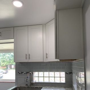 White kitchen cabinets above a sink and tiled backsplash.