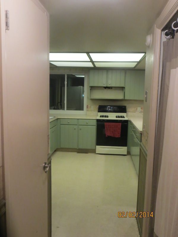 View of a green kitchen from a doorway. Cabinets, stove, and window are visible.