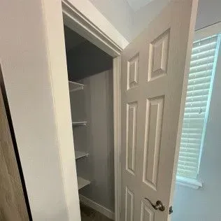 White interior door ajar, revealing a closet with shelves. A window with blinds is visible.