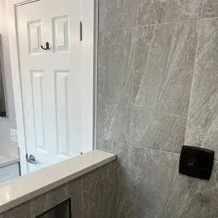 White bathroom door next to a gray tiled shower wall with a black control panel.