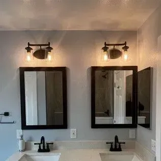 Two bathroom vanities with black framed mirrors and sconce lighting.