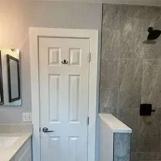 White bathroom door with hooks, beside a gray tiled shower.