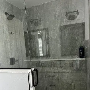 Bathroom with gray marble walls, glass shower door, and vanity with mirror.